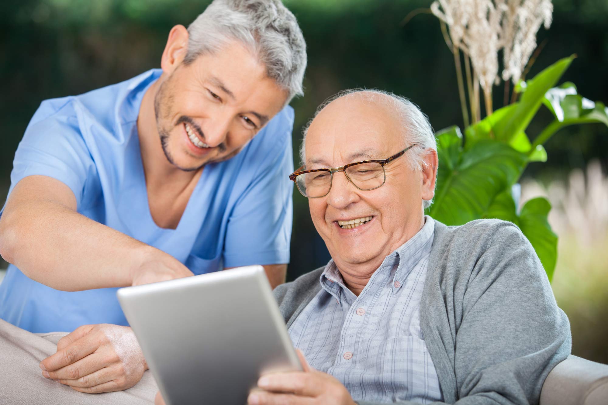 Krankenpfleer und älterer Mann genießen die Verwendung eines Tablet-Computers: © Tyler Olson – stock.adobe.com